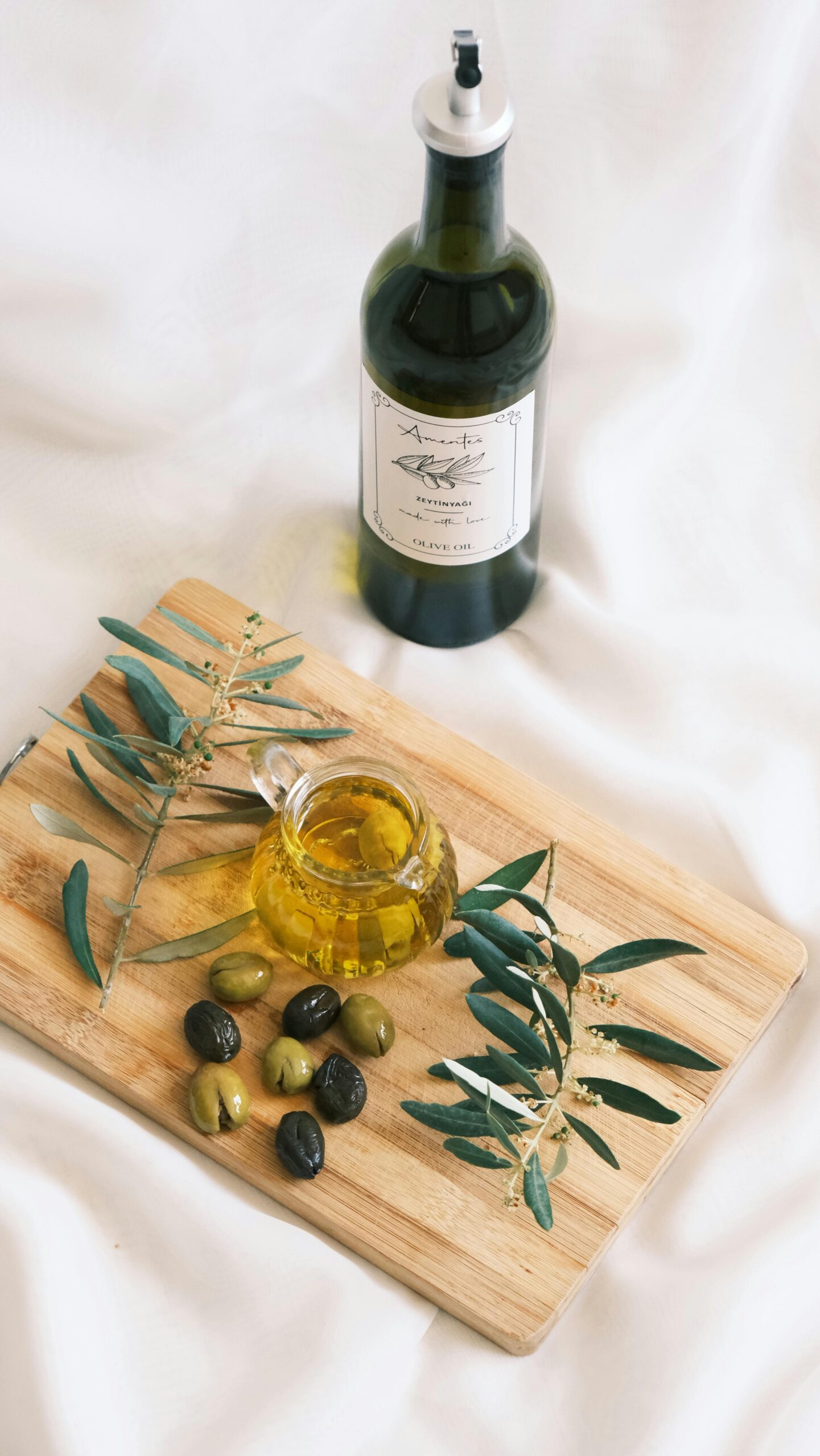 pexels photo 25745504 25745504 Stylish arrangement of olive oil bottle, olives, and olive branches on a wooden board.